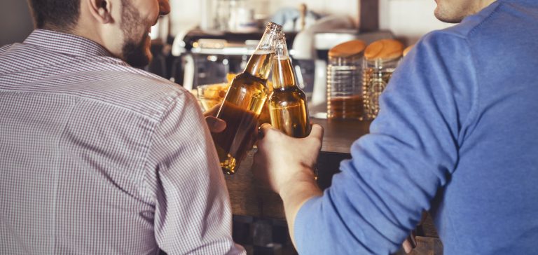 Mates Clinking Bottles Of Beer In Pub